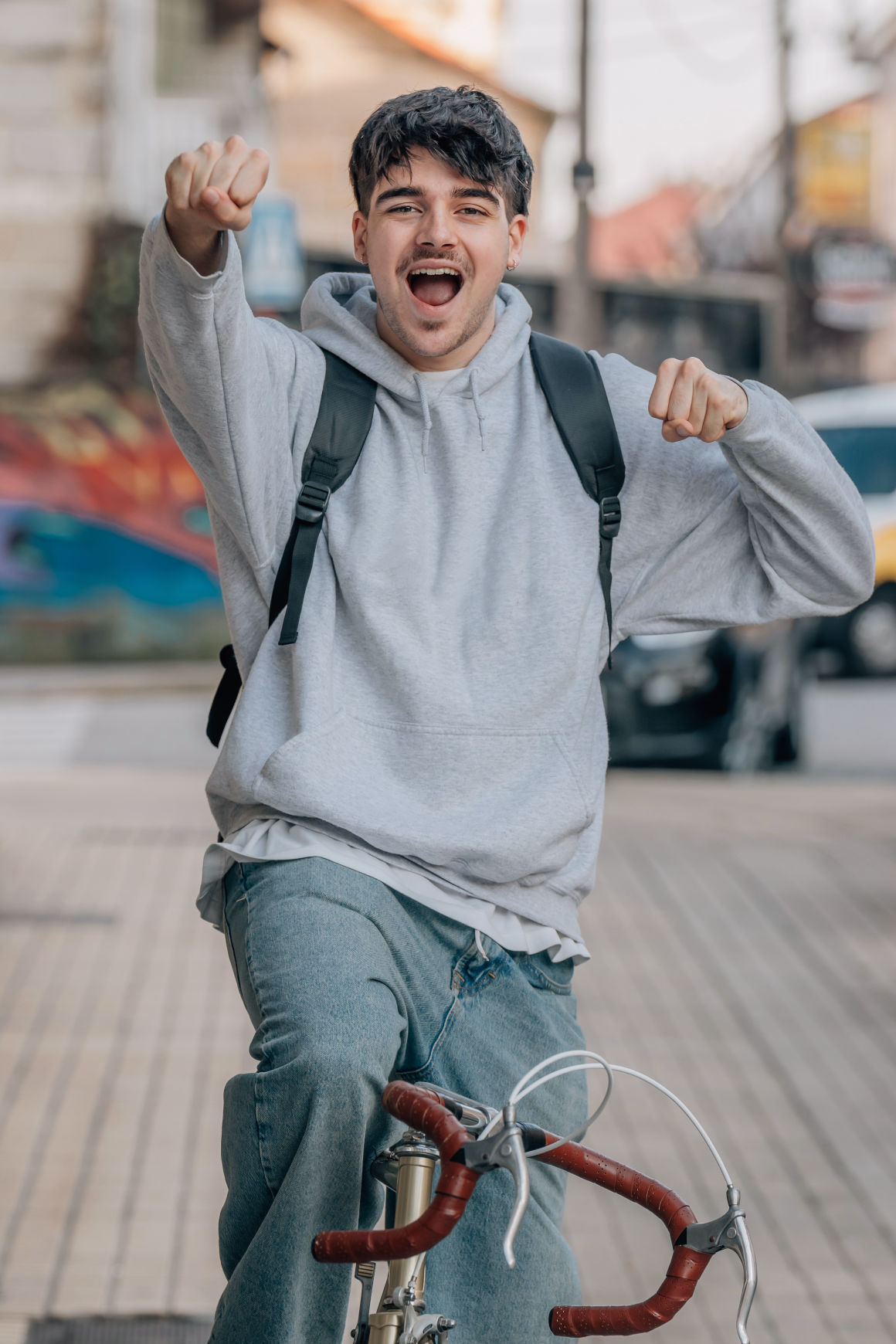 A young man on a bicycle, arms raised in celebration on a city street — the kind of forward-looking energy Project S.A.F.E. is designed to support.